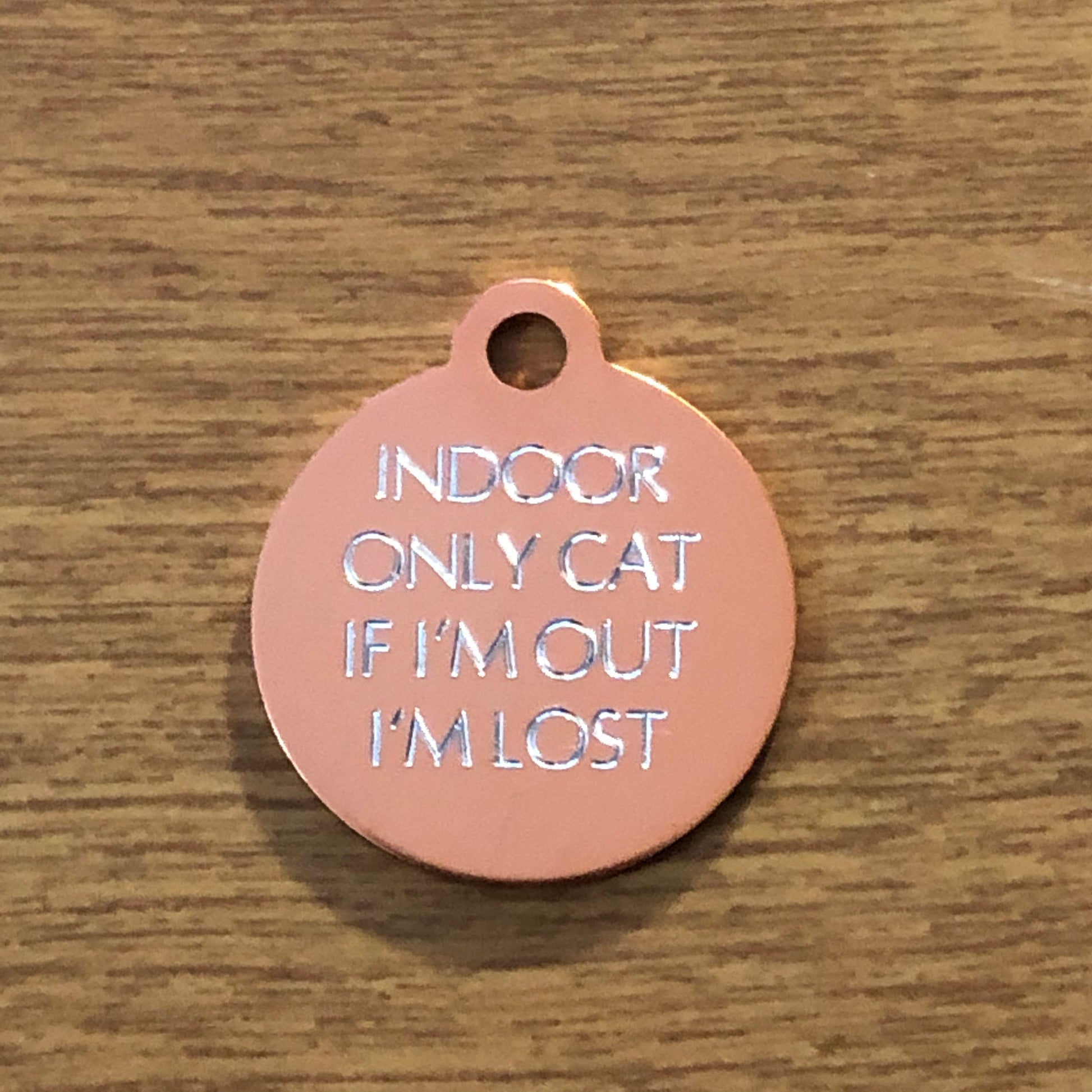 Small rose gold circle tag that says: Indoor only cat If I'm out I'm lost. All engraved in capital letters.