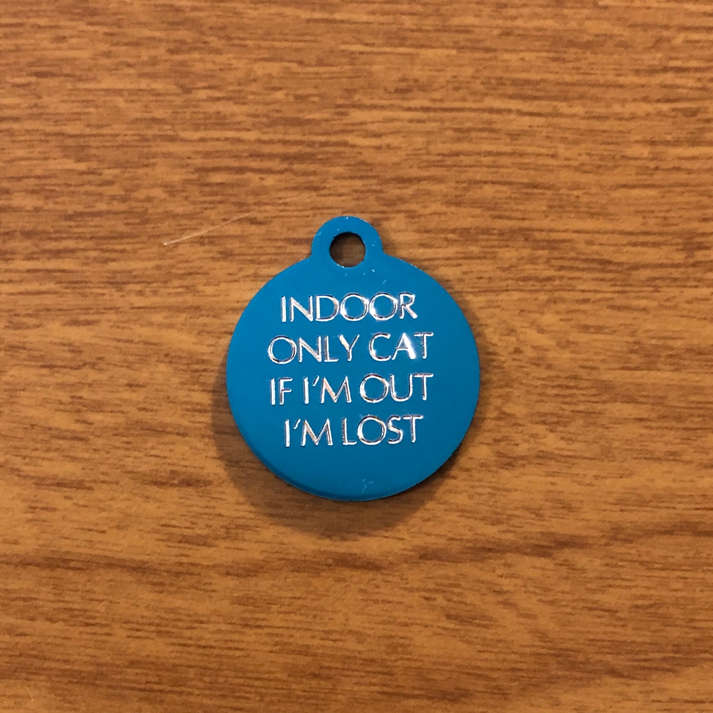 Small turquoise circle tag that says: Indoor only cat If I'm out I'm lost. All engraved in capital letters.