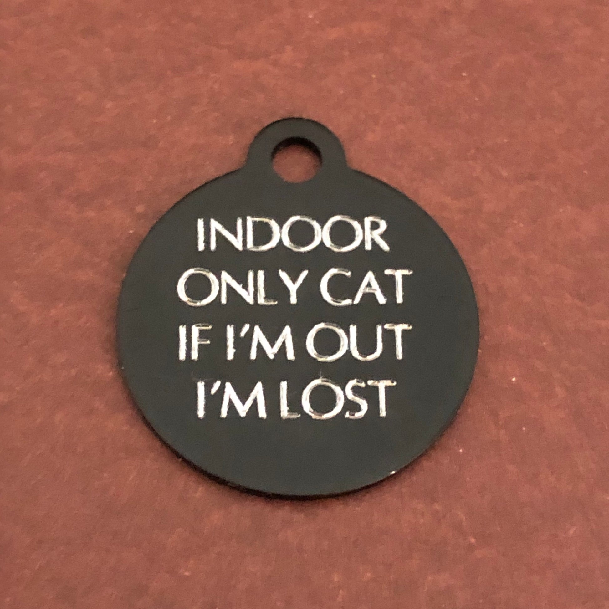 Small black circle tag that says: Indoor only cat If I'm out I'm lost. All engraved in capital letters.