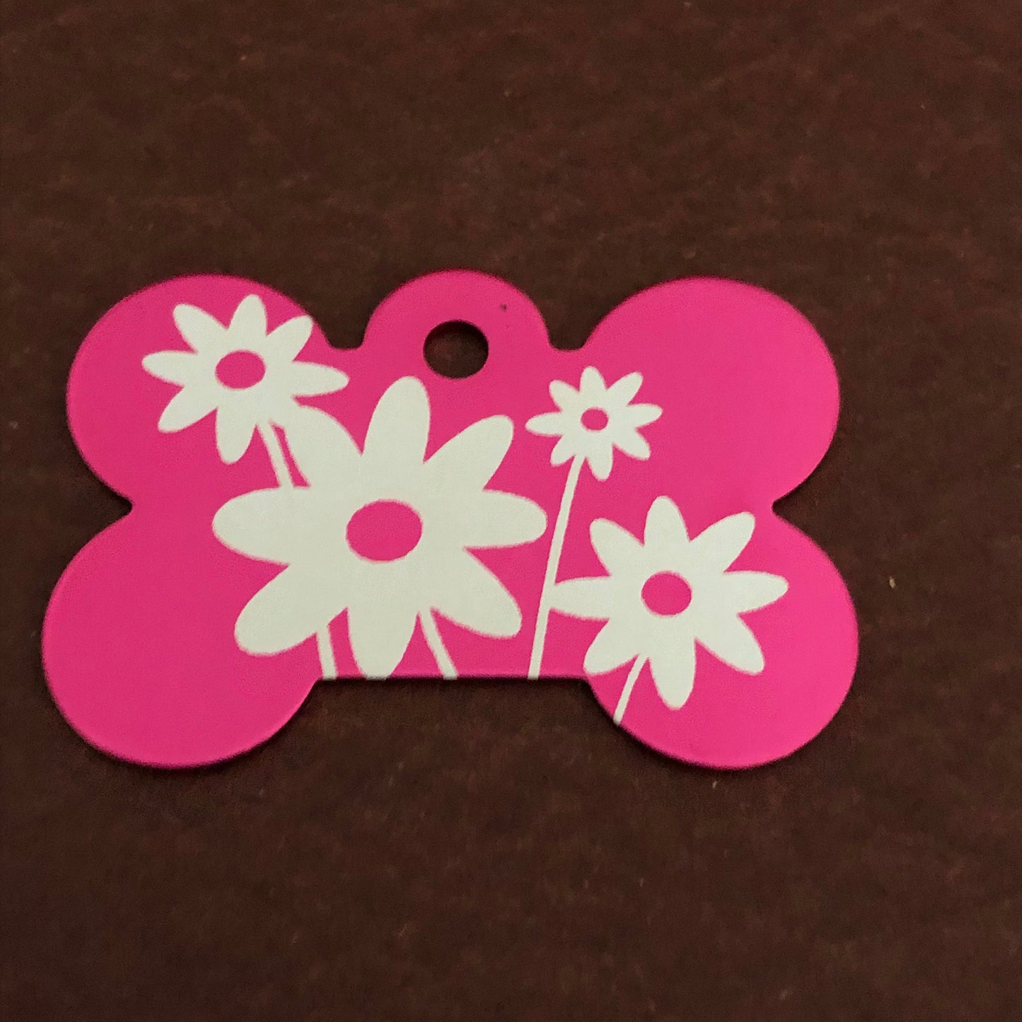 It is a large pink aluminum bone tag with a daisy floral design on it.
The Tag measures approximately 1 9/16"W x 1 1/16"H.