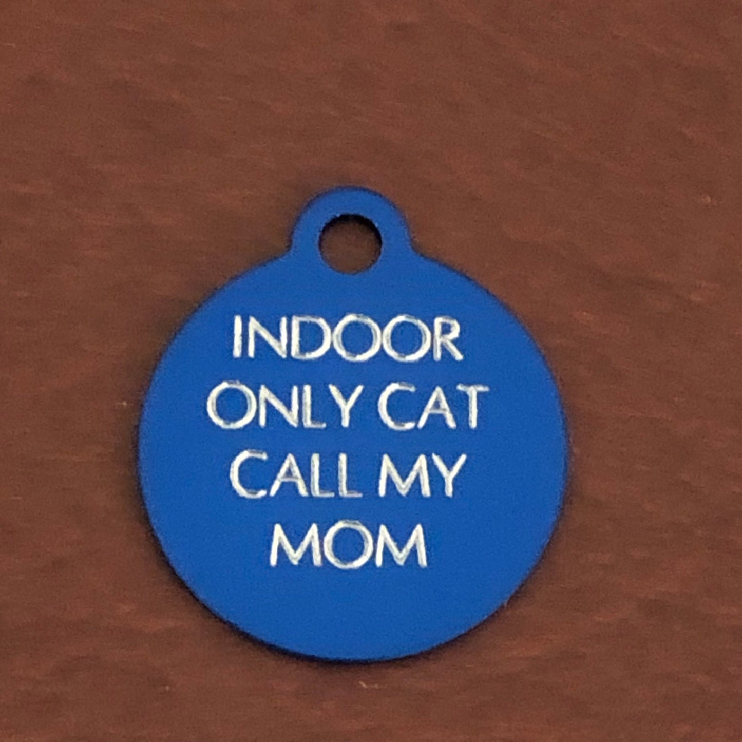 Small blue circle tag that says: Indoor only cat call my mom. All engraved in capital letters.