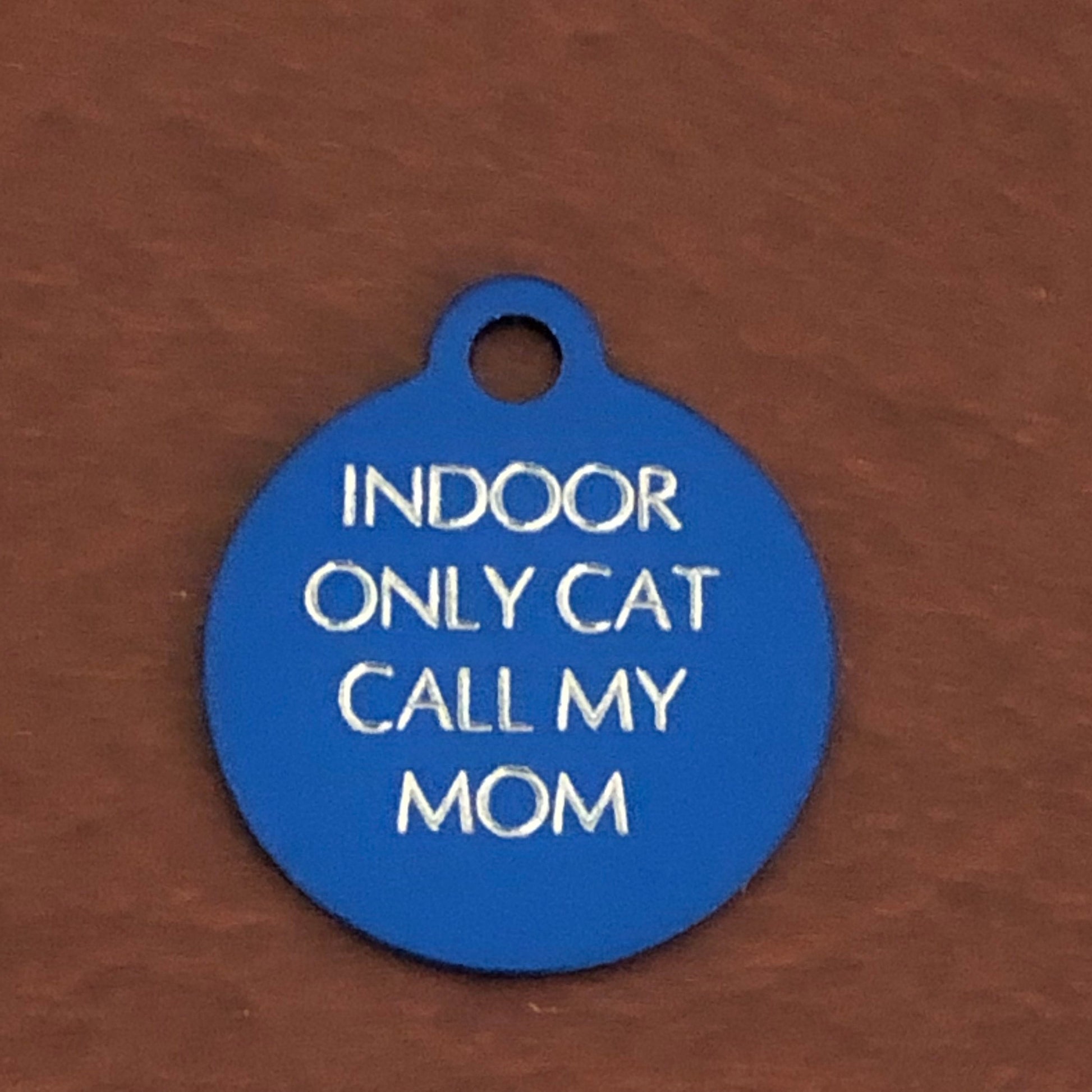 Small blue circle tag that says: Indoor only cat call my mom. All engraved in capital letters.