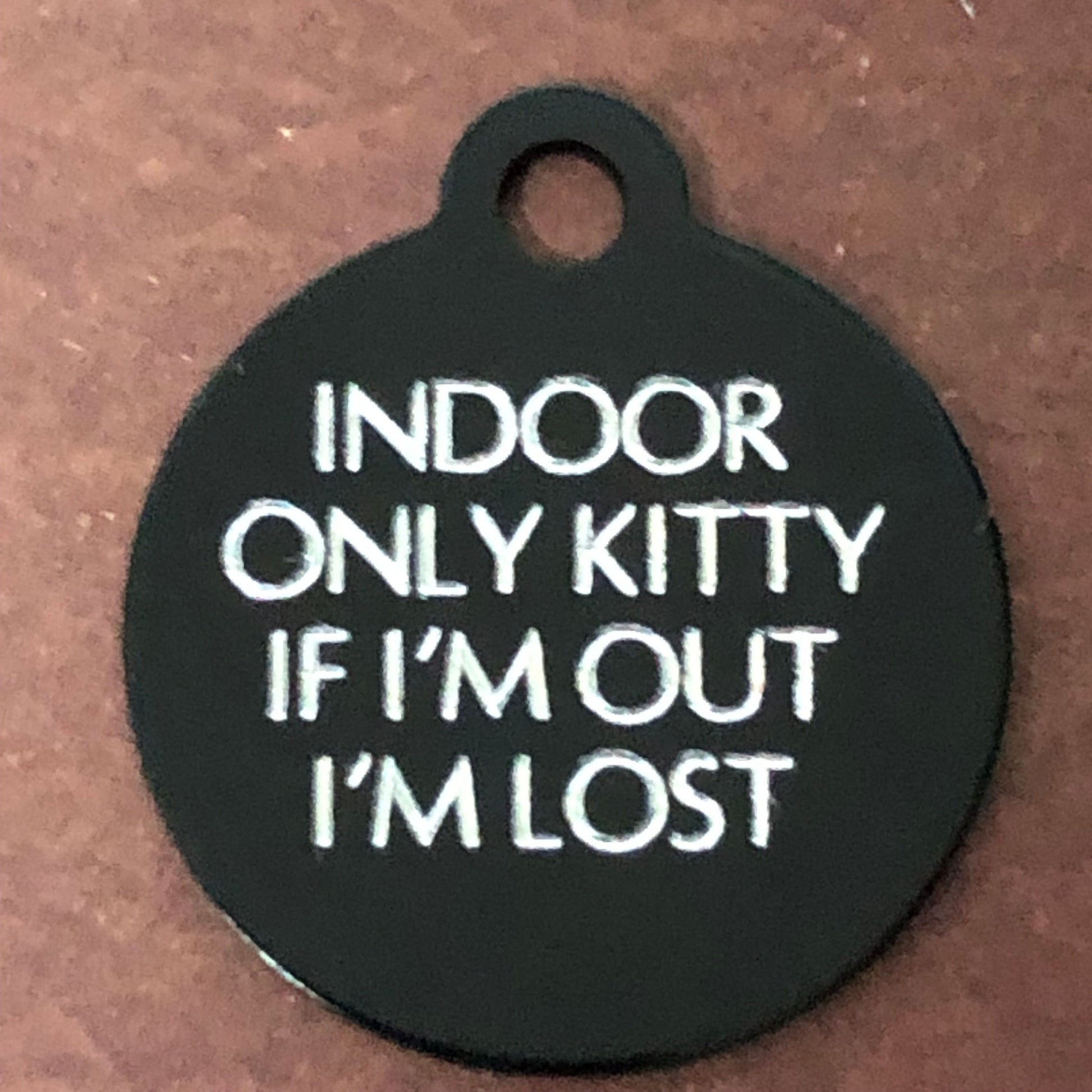 Small black circle tag that says: Indoor only kitty If I'm out I'm lost. All engraved in capital letters.
