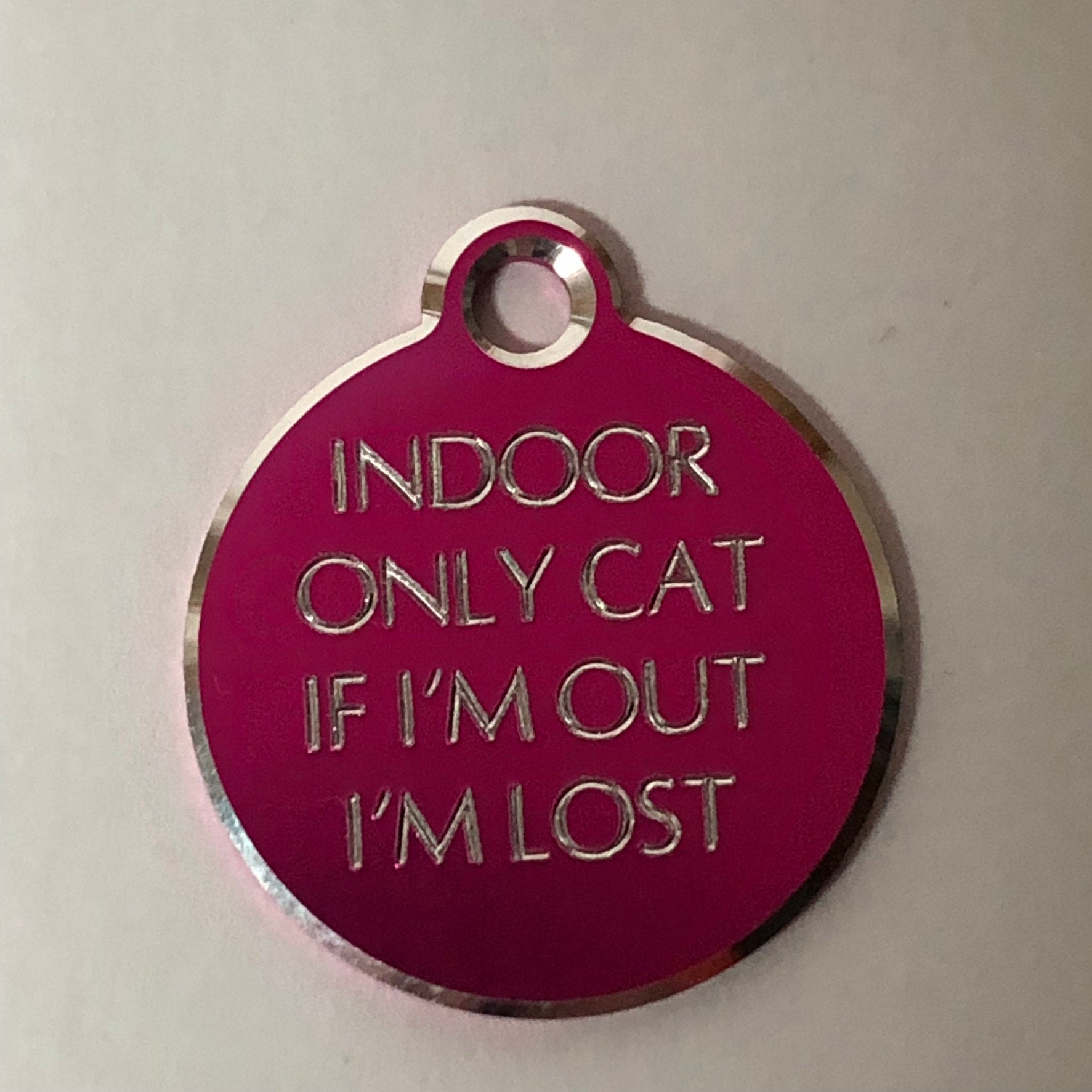 Small Hi-LITE pink circle tag that says: Indoor only cat If I'm out I'm lost. All engraved in capital letters.