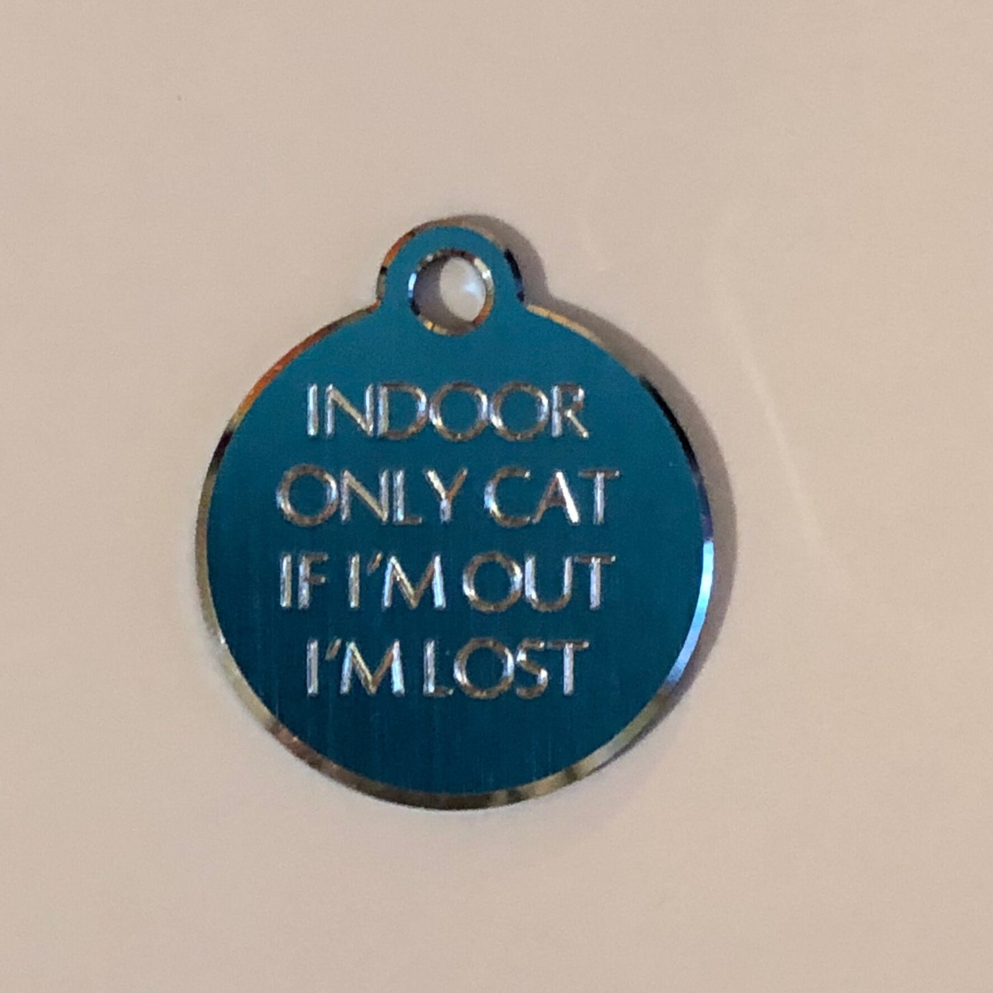 Small Hi-LITE blue circle tag that says: Indoor only cat If I'm out I'm lost. All engraved in capital letters.