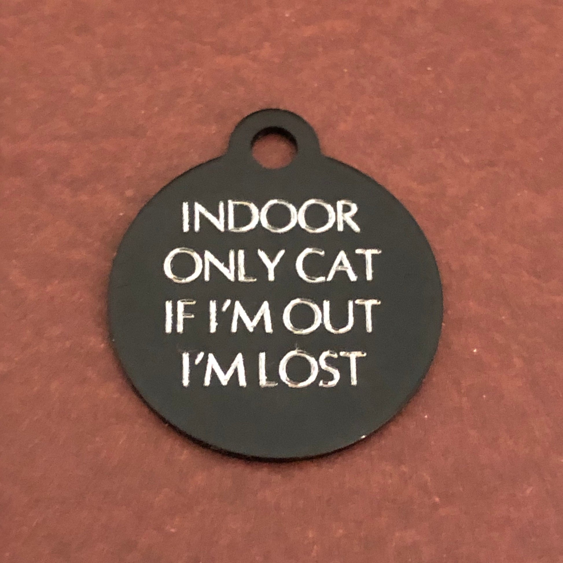 Small black circle tag that says: Indoor only cat If I'm out I'm lost. All engraved in capital letters.