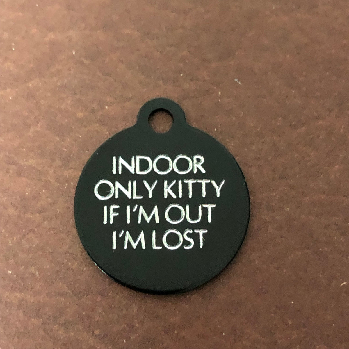 Small black circle tag that says: Indoor only kitty If I'm out I'm lost. All engraved in capital letters.